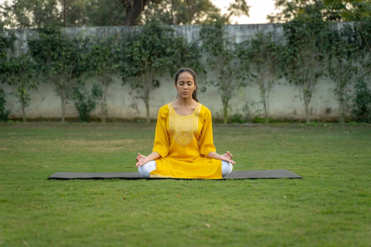 Woman in yellow dress meditating on a yoga mat outdoors